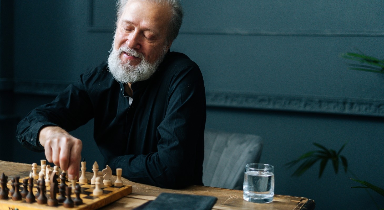 Portrait of happy bearded mature male performing move with pawn piece on wooden chessboard