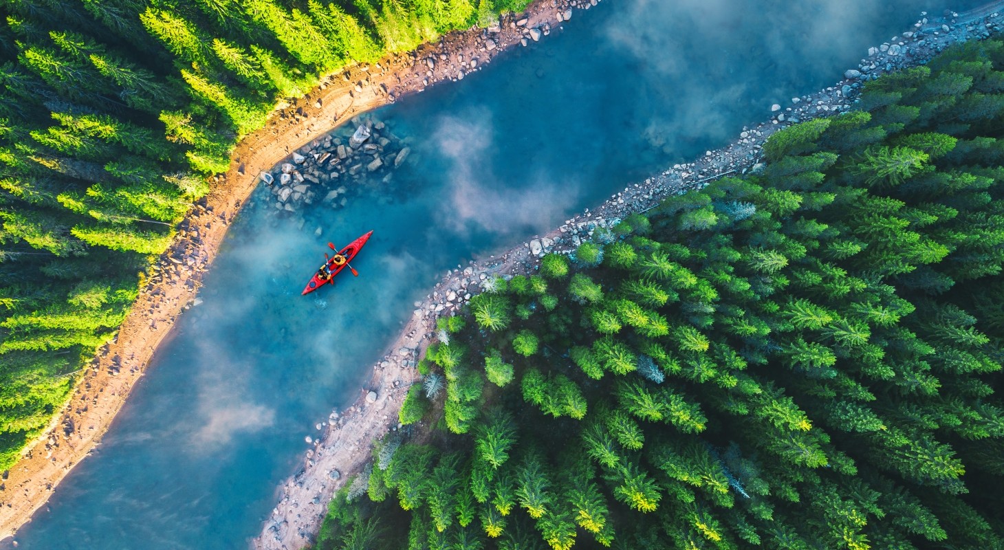 aerial view of red kayak on blue river between green forests 