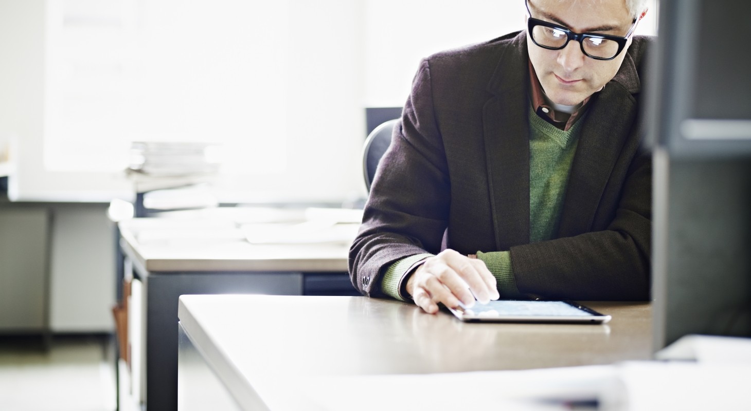 man with graying hair and glasses in suit jacked checking ipad