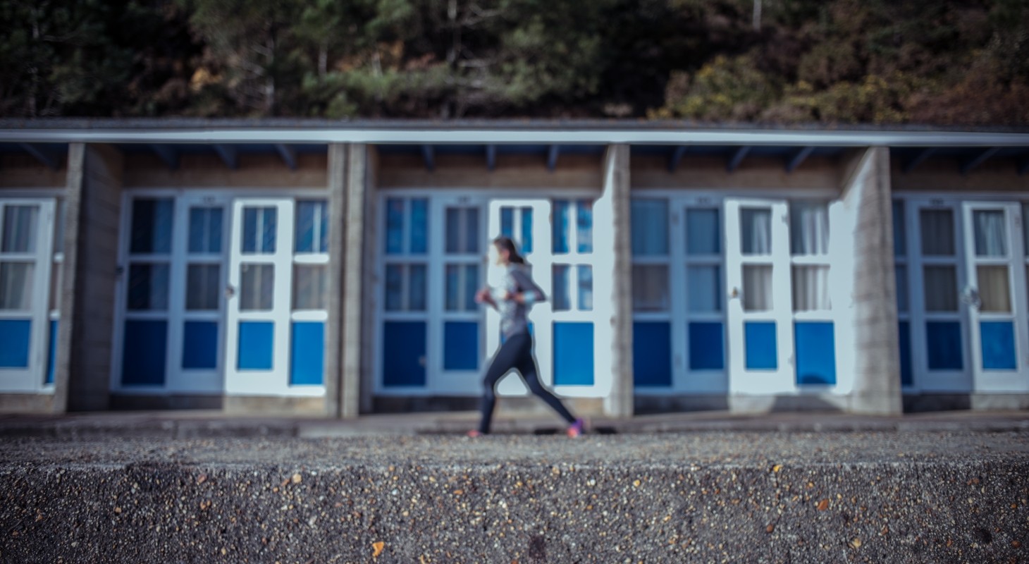 blurred focus of female runner on beach in front of low condos with blue doors