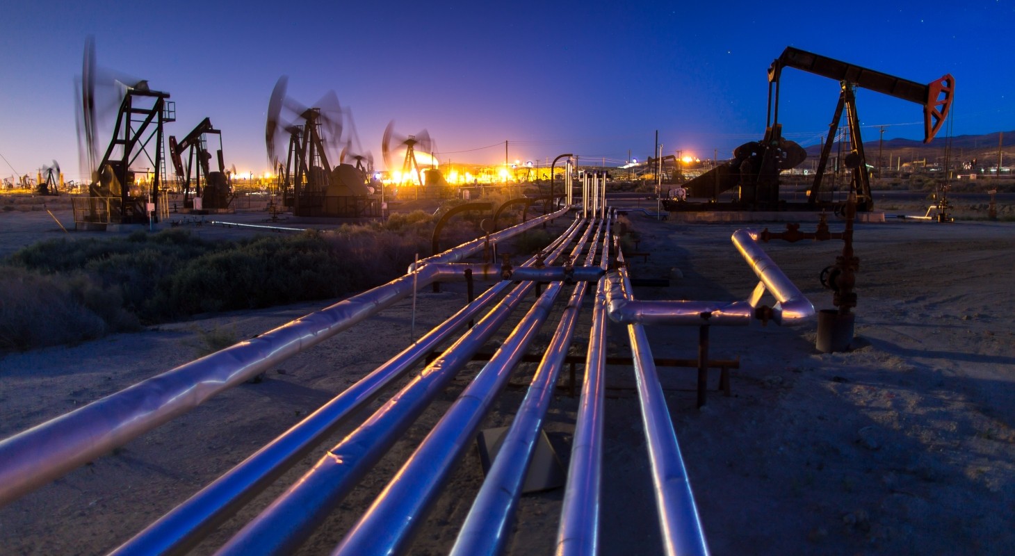 multiple pumpjacks illuminated against evening sky