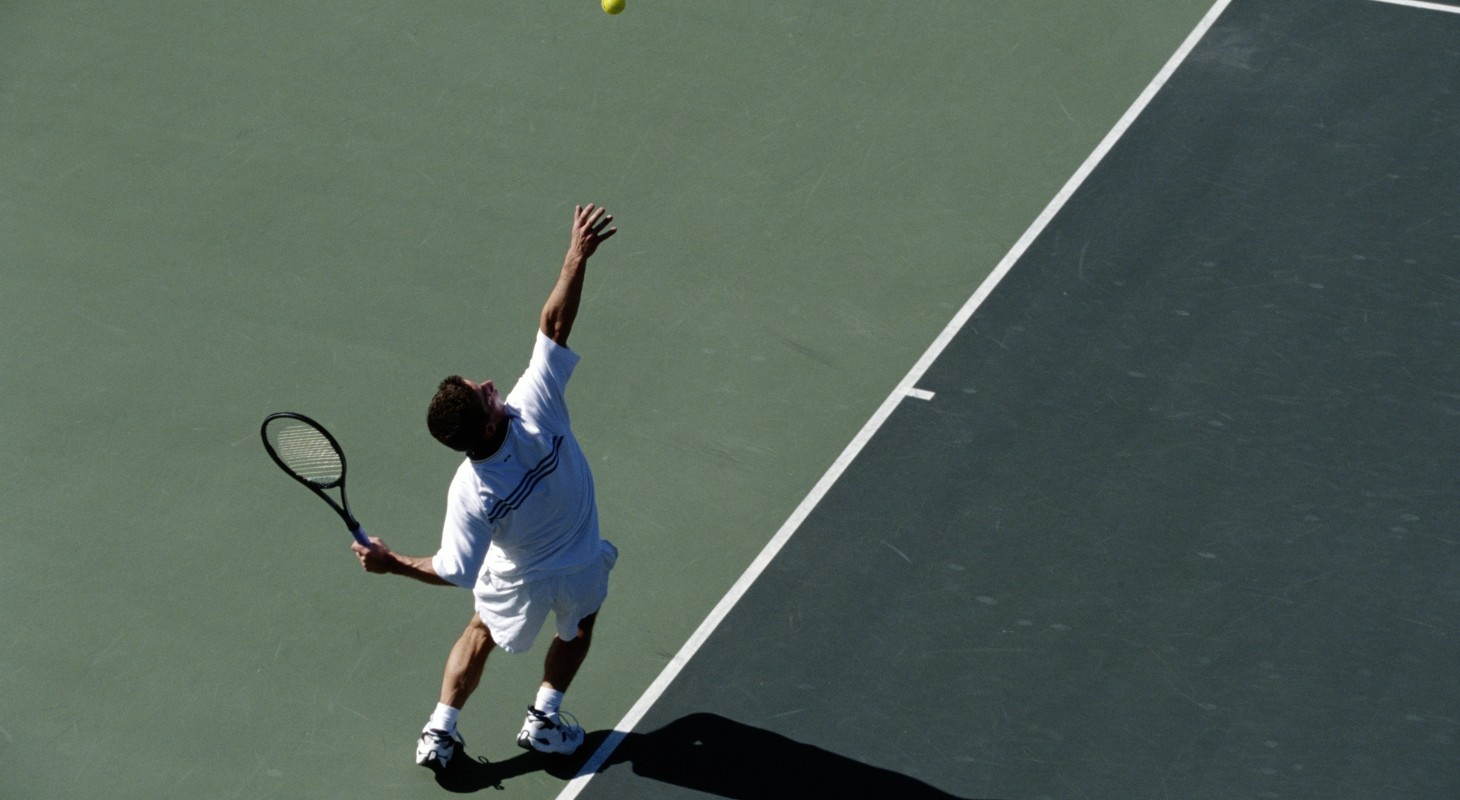 male tennis player serving on dark gray and green court