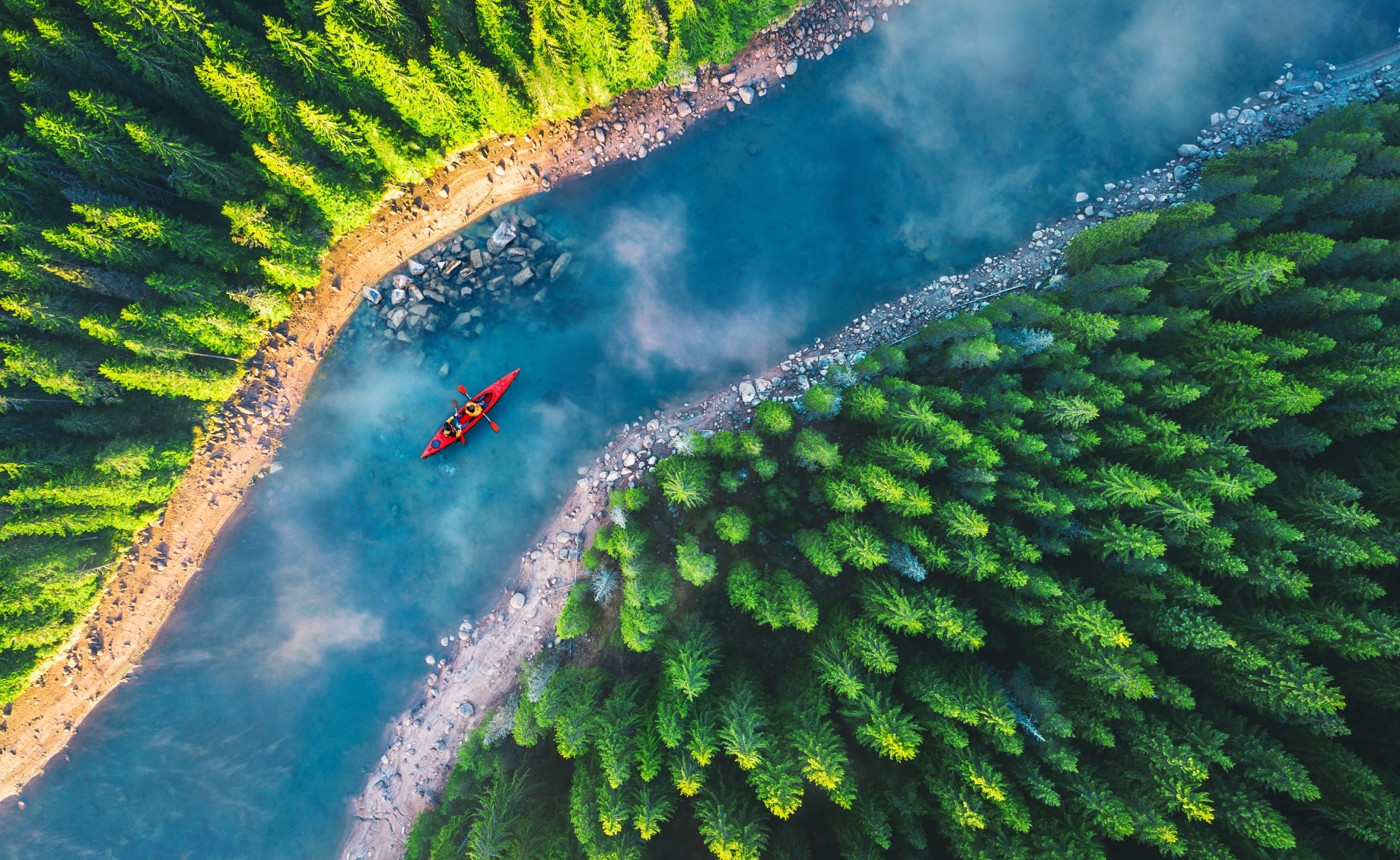 aerial view of red kayak on blue river between green forests 