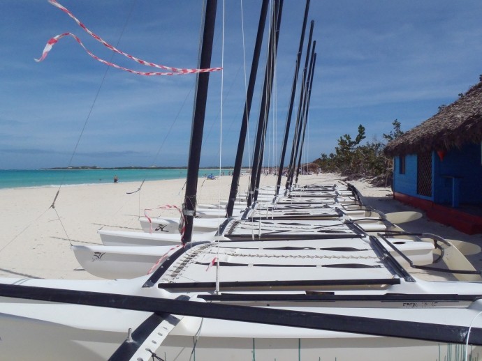 hobie cat sailboats without sails lined up on white beach