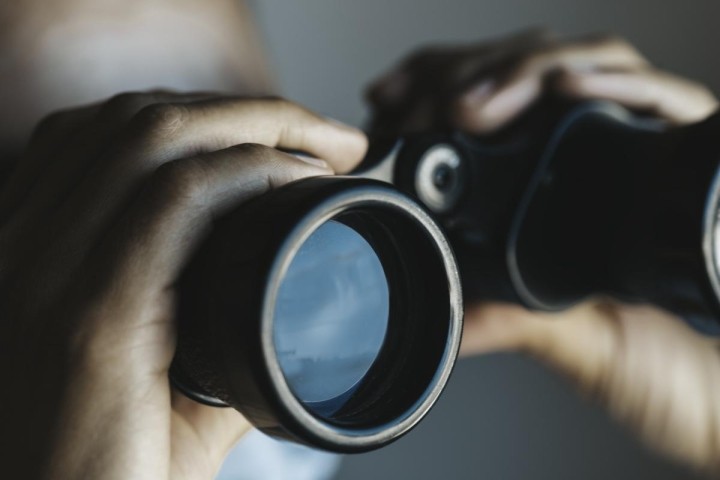 close-up of hands holding binoculars with blue sky reflecting in lens