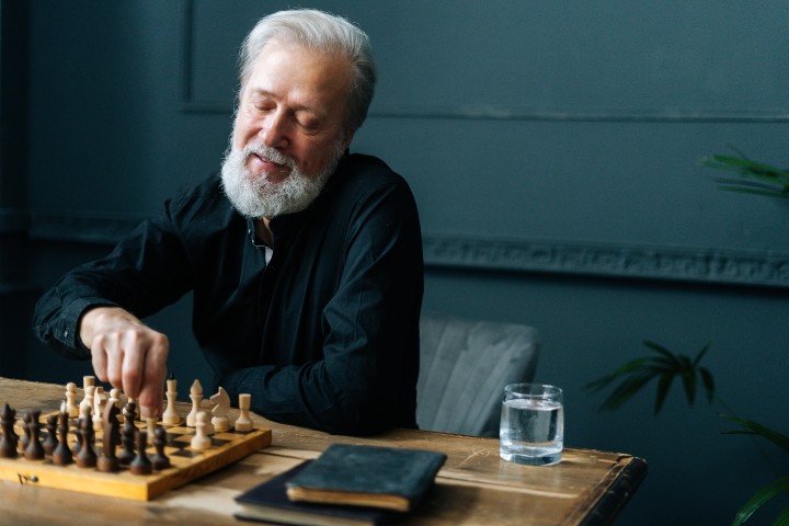 Portrait of happy bearded mature male performing move with pawn piece on wooden chessboard