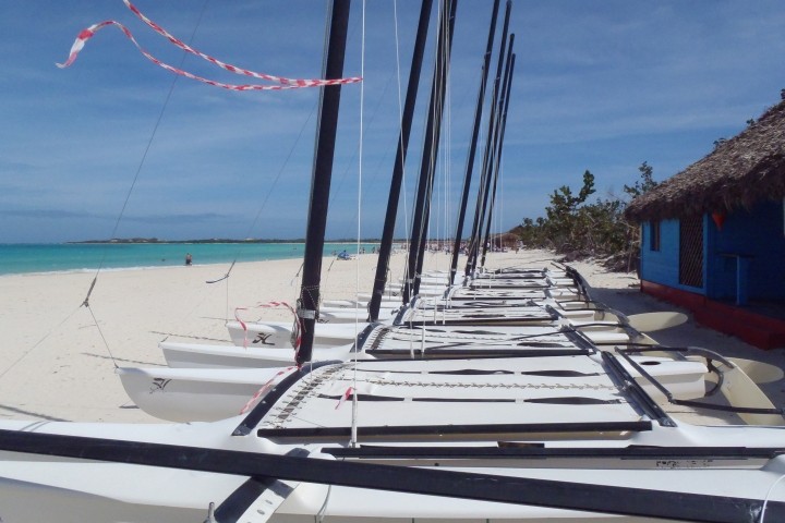 hobie cat sailboats without sails lined up on white beach