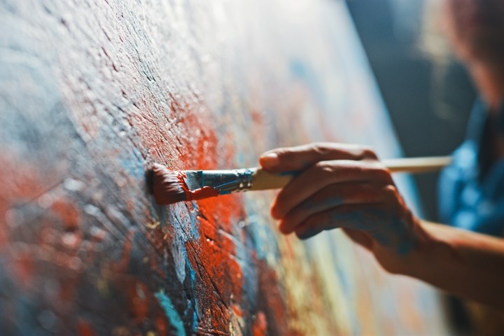 older female artist paints on closeup of red and blue canvas