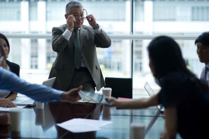 board meeting with director standing up and putting on glasses