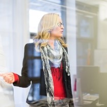 woman in glasses red sweater and black jacket leading a conference room discussion