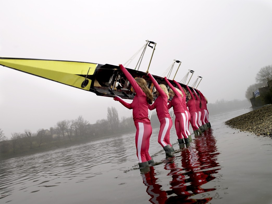 female rowers standing in lake carrying eight person scull